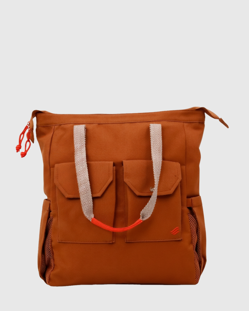 Rustic Caramel (R)evolution™ 27L Utility Convertible Tote (Front): Rust-orange canvas tote with herringbone handles, front flap pockets, red zipper pull