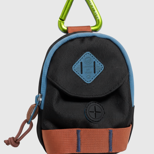 Black Multi (R)evolution™ Dog Waste Bag Dispenser (Angle): Mini backpack-shaped dispenser, black canvas, blue trim, brown strap, green carabiner