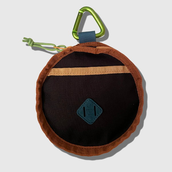 Black (R)evolution™ Collapsible Double Dog Bowl (Front): Round black pouch with rust trim, tan pocket stripe, teal logo patch, green carabiner