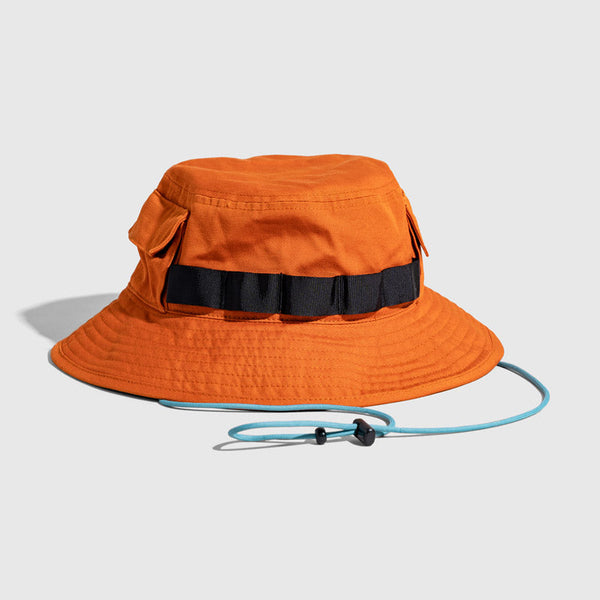 Tangerine Organic Bucket Stash Hat (Angle): Rust-orange boonie hat with black webbing band, side pocket, and teal chin cord
