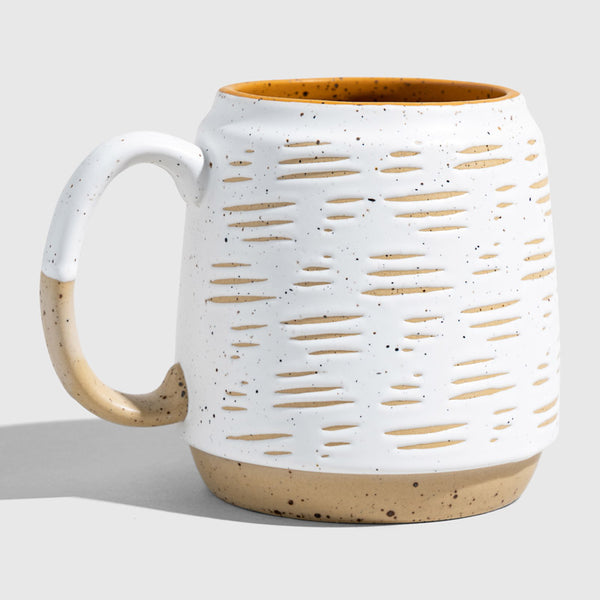 Eggshell 16 oz. Stoneware Mug (Angle): White speckled mug with carved dash pattern, tan base, mustard interior