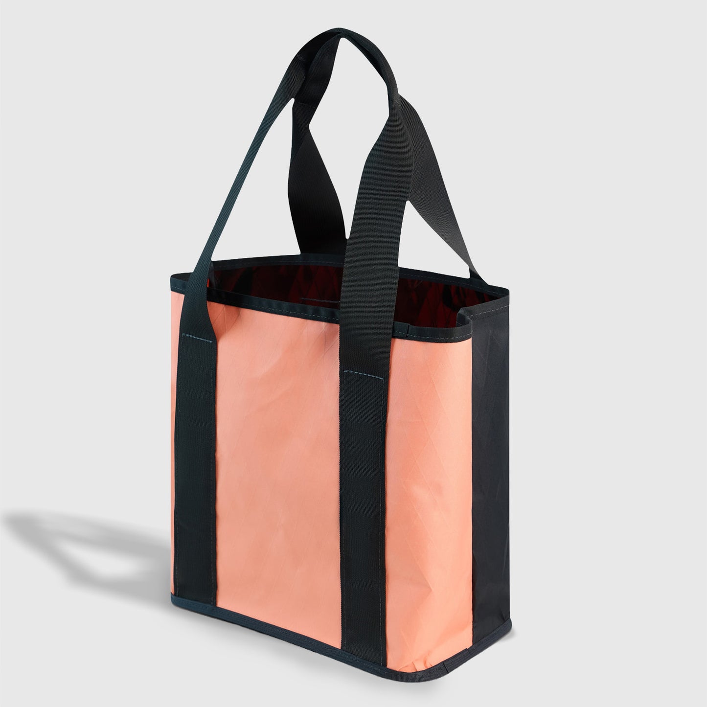 Peach-Navy The Westward Tote (Angle): Salmon-colored tote with dark navy webbing straps, trim, and open top