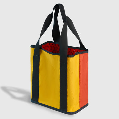 Coral Red The Westward Tote (Angle): Yellow and orange tote with dark straps and red quilted interior visible