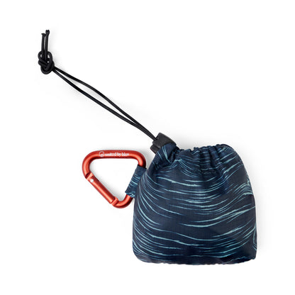 Waves The Packable Tote (Packed): Navy wave-print tote folded into stuff sack with red carabiner clip and black bungee toggle