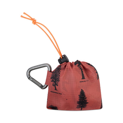 Clay The Packable Tote (Packed): Rust-orange tree-print tote folded into stuff sack with silver carabiner clip and orange bungee toggle