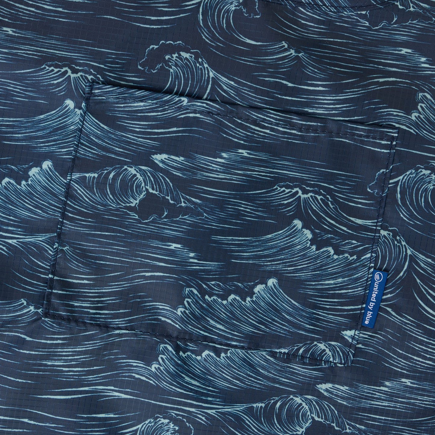 Waves The Packable Tote (Detail): Close-up of navy fabric printed with hand-drawn ocean wave illustrations and front pocket seam
