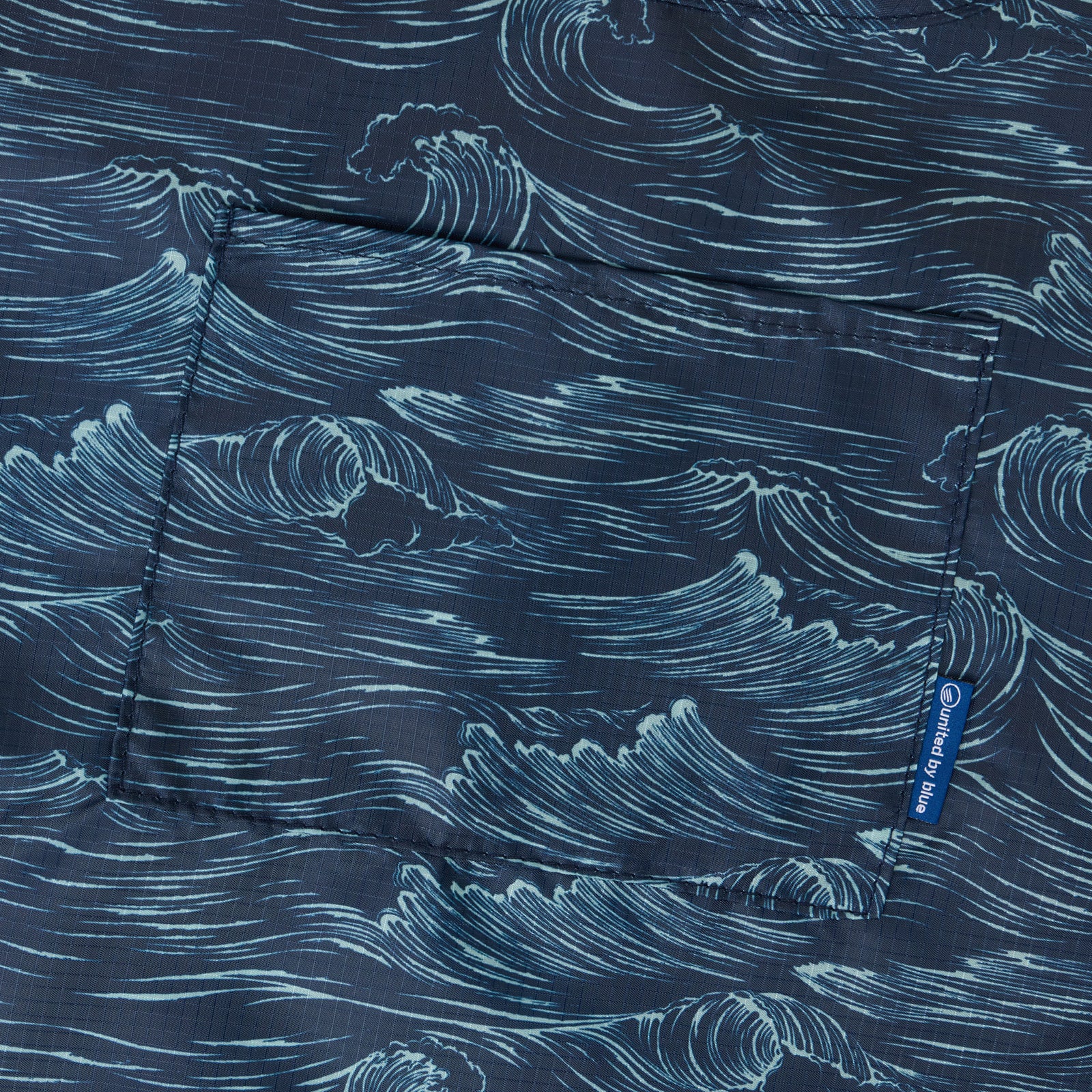 Waves The Packable Tote (Detail): Close-up of navy fabric printed with hand-drawn ocean wave illustrations and front pocket seam