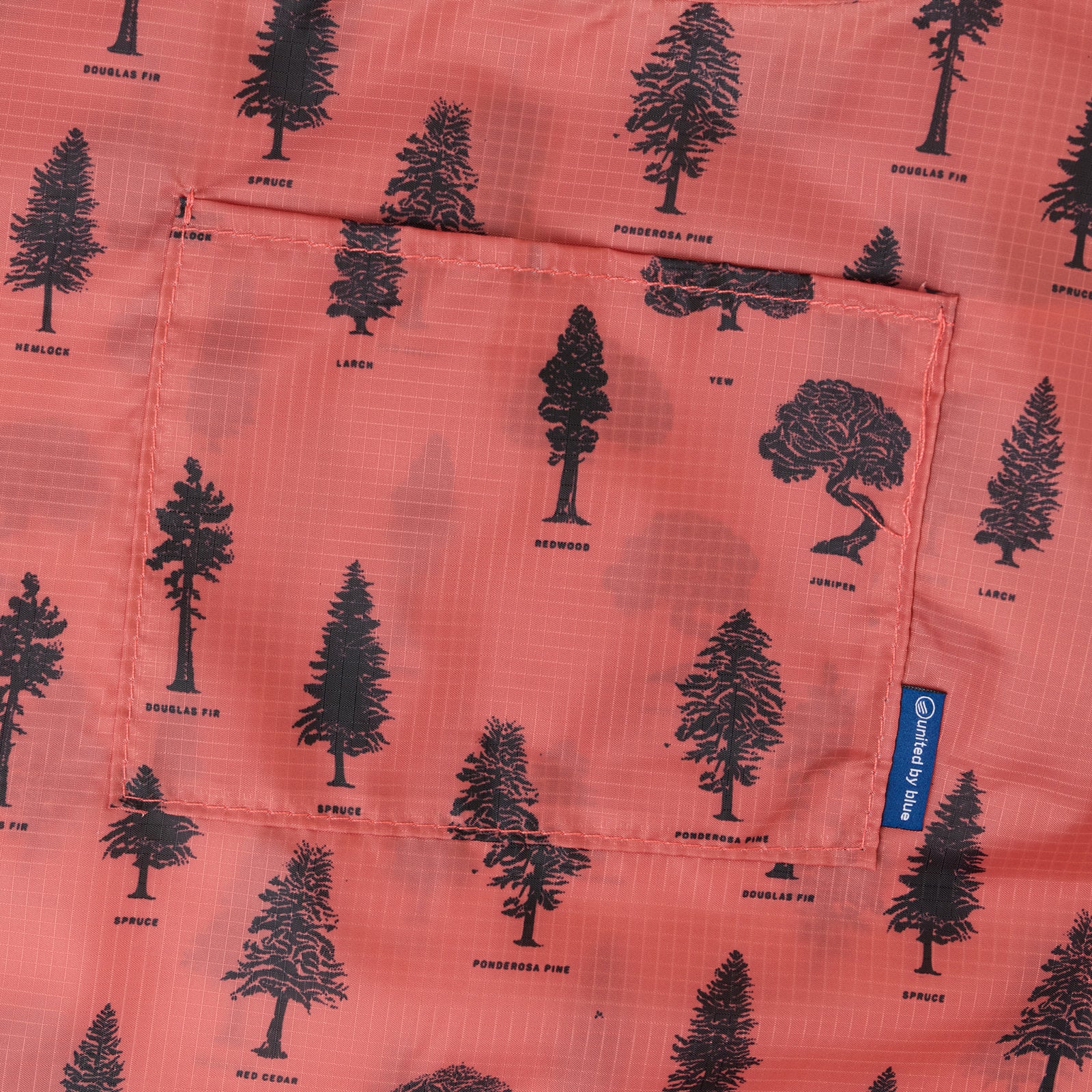 Clay The Packable Tote (Detail): Close-up of rust-orange fabric with labeled black tree silhouettes including Douglas Fir and Ponderosa Pine