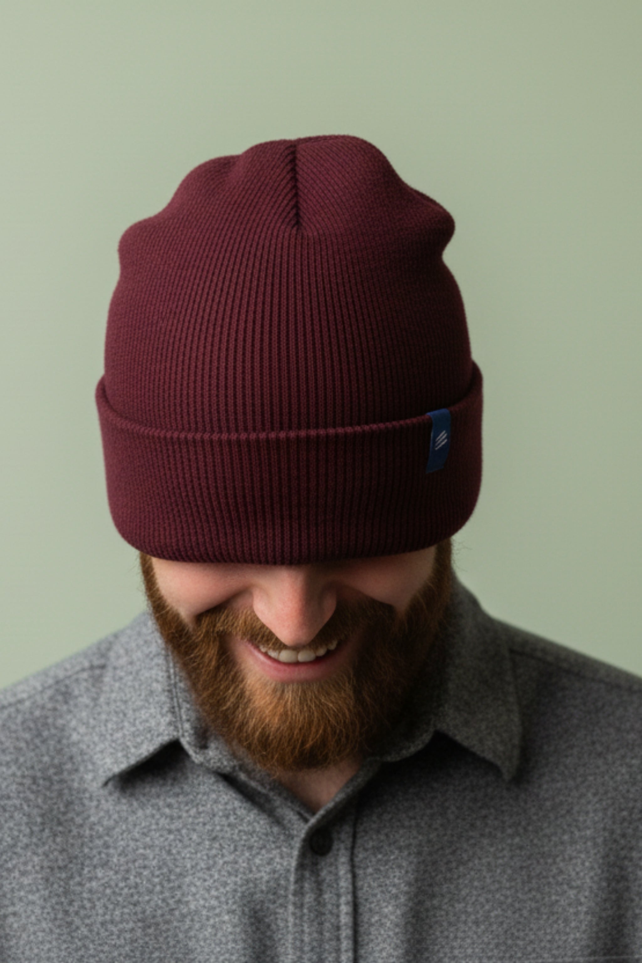 Man wearing a maroon beanie with a logo on a light green background