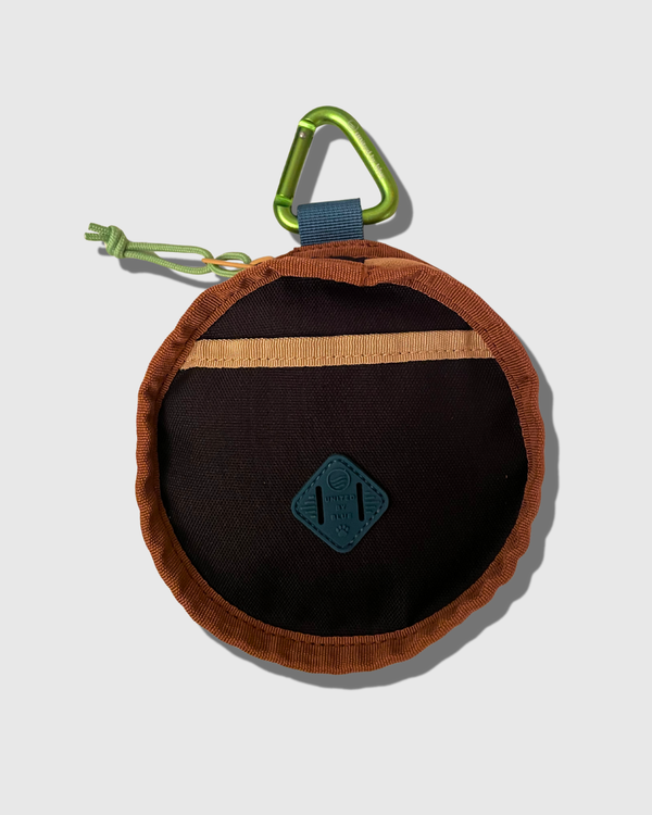 Black (R)evolution™ Collapsible Double Dog Bowl (Front): Round black pouch with rust trim, tan pocket stripe, teal logo patch, green carabiner