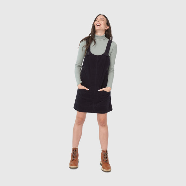 Night Sky Corduroy Overall Dress (In-use): Dark corduroy pinafore dress with straps, pockets, worn over sage turtleneck