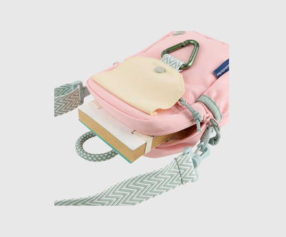 Lt Pink (R)evolution Daily Cross Body (Detail): Pink bag with snap-flap open showing notebook inside, green carabiner, and chevron shoulder strap