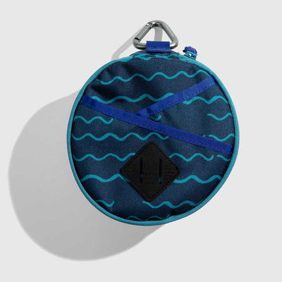 Navy The Meal Kit (Single) (Front): Round navy pouch with teal wave print, crossed blue straps, carabiner clip