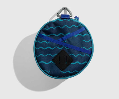 Navy The Meal Kit (Single) (Front): Round navy pouch with teal wave print, blue cross straps, carabiner clip
