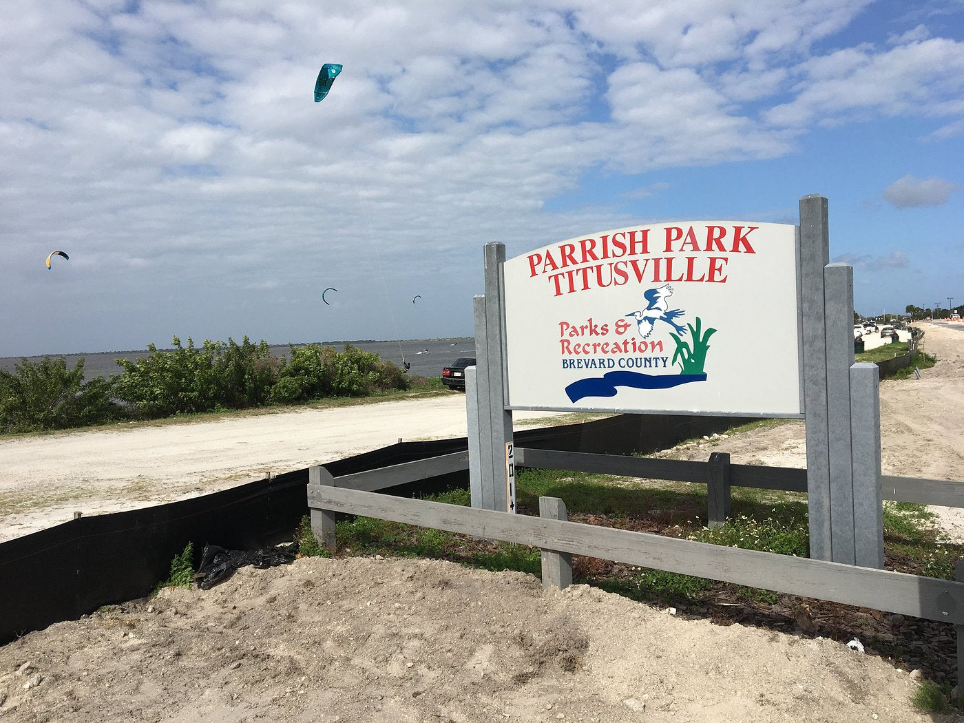 Parrish Park sign on the Indian River Lagoon in Titusville, Florida, with kitesurfers on the water in the background