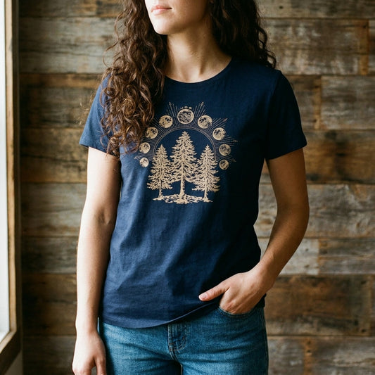 navy Womens Fit Graphic Tee in 100% Organic Cotton - Lunar Phases (In-use): Woman wearing dark blue tee with gold pine trees and moon phases graphic
