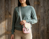 Lt Pink Bag - Person wearing a green sweater and beige pants with a pink crossbody bag against a wooden background