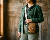 Tigers Eye Bag - Person wearing a green jacket holding a brown crossbody bag against a wooden wall.