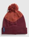 EGGPLANT Recycled Chevron Pom Beanie (Flat-lay): Deep burgundy knit beanie with orange chevron pattern and pom-pom top