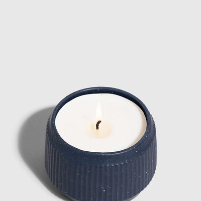 INDIGO 14 oz. Ceramic Keepsake Candle - Surf (Angle): Short navy ridged ceramic vessel holds white wax with lit wick