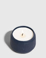 INDIGO 14 oz. Ceramic Keepsake Candle - Surf (Angle): Navy blue ribbed ceramic vessel with white wax candle and lit wick