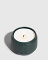 DARK GREEN 14 oz. Ceramic Keepsake Candle - Tioga Woods (Angle): Round dark teal ribbed ceramic vessel holding white wax with lit wick