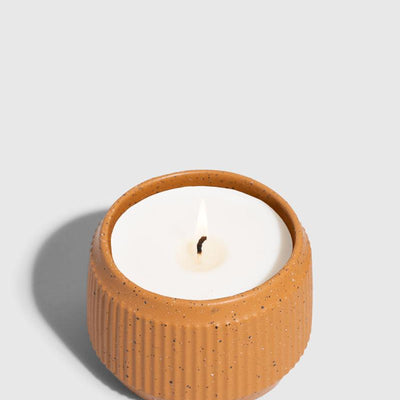 CARAMEL 14 oz. Ceramic Keepsake Candle - Mountain Peak (Angle): Round ribbed speckled terracotta ceramic vessel holding white wax candle, lit wick