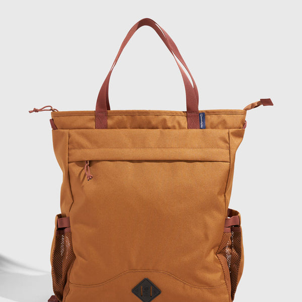 Camel (R)evolution™ 25L Convertible Carryall (Front): Tan tote bag with rust straps, front zip pocket, mesh side pockets