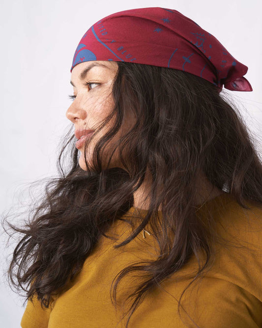 Organic Bandana (In-use): Crimson bandana with blue graphic print tied around dark-haired woman's head