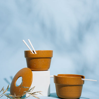 Caramel Stoneware Stackable Noodle Bowl Set (Angle): Two speckled amber bowls with ribbed bases, white chopsticks, and donut lid