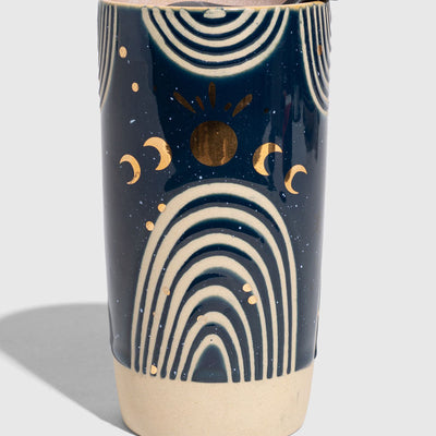 Nightfall Blue 10 oz. Insulated Stoneware Travel Mug (Angle): Navy blue ceramic tumbler with gold moons, sun, and cream arch designs