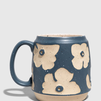 Eclipse Blue 16 oz. Stoneware Mug (Angle): Barrel-shaped mug with raised cream floral shapes on matte blue speckled glaze