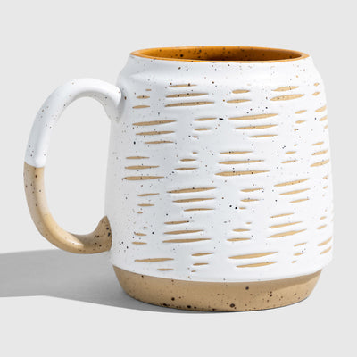 Eggshell 16 oz. Stoneware Mug (Angle): White speckled mug with oval cutout texture, tan base, mustard interior