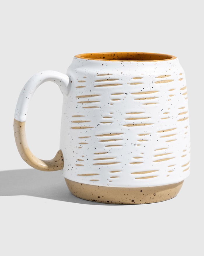 Eggshell 16 oz. Stoneware Mug (Angle): White speckled mug with oval cutout texture, tan base, mustard interior