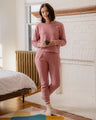 Foxglove EcoKnit™ Seamed Sweatpant (In-use): Woman in dusty rose matching set holds mug in bright bedroom