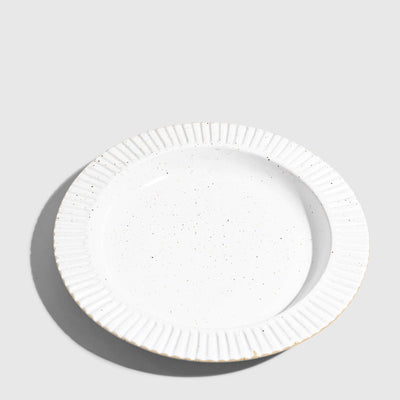 Eggshell Stoneware Stackable Plate (Angle): Round white speckled plate with ribbed fluted rim, unglazed edge visible